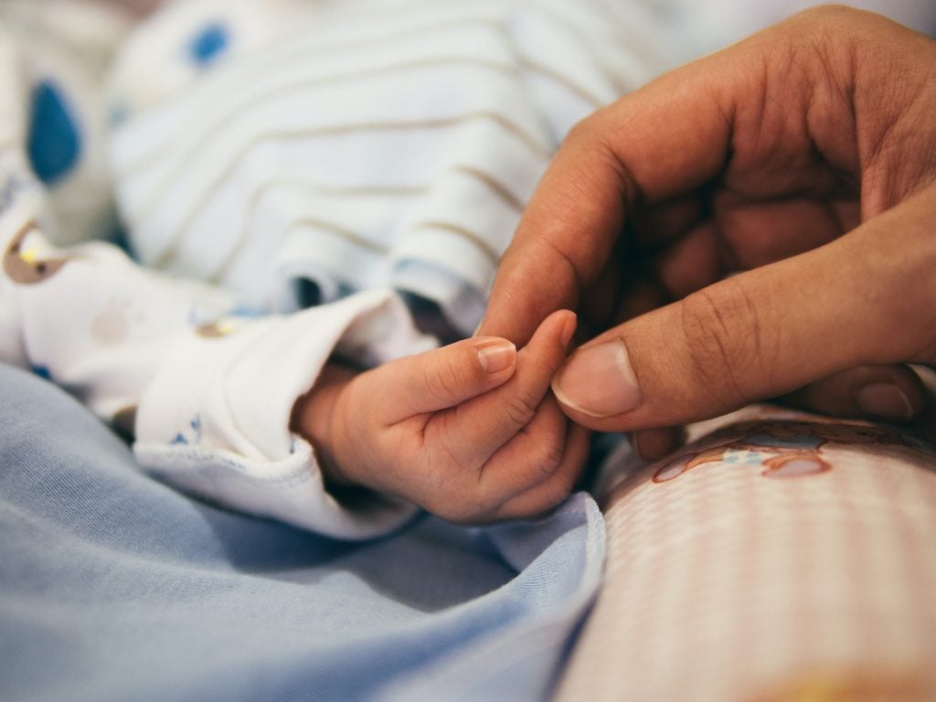 Newborn baby holding an adult finger