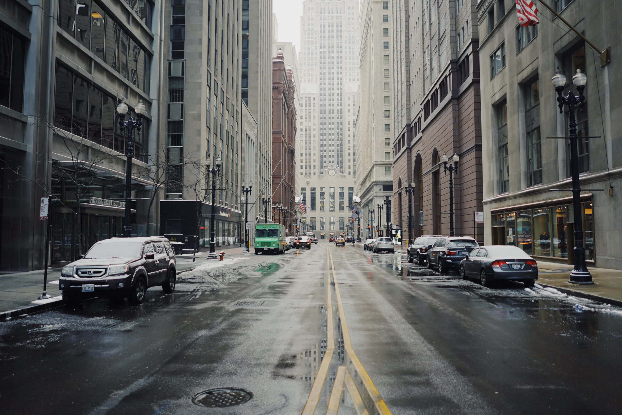 Wet city street with cars and buildings on a snowy day
