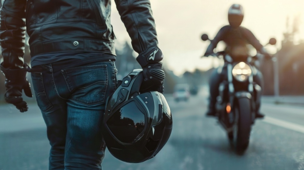 Motorcycle helmet laws emphasized as rider walks with helmet while another motorcycle passes