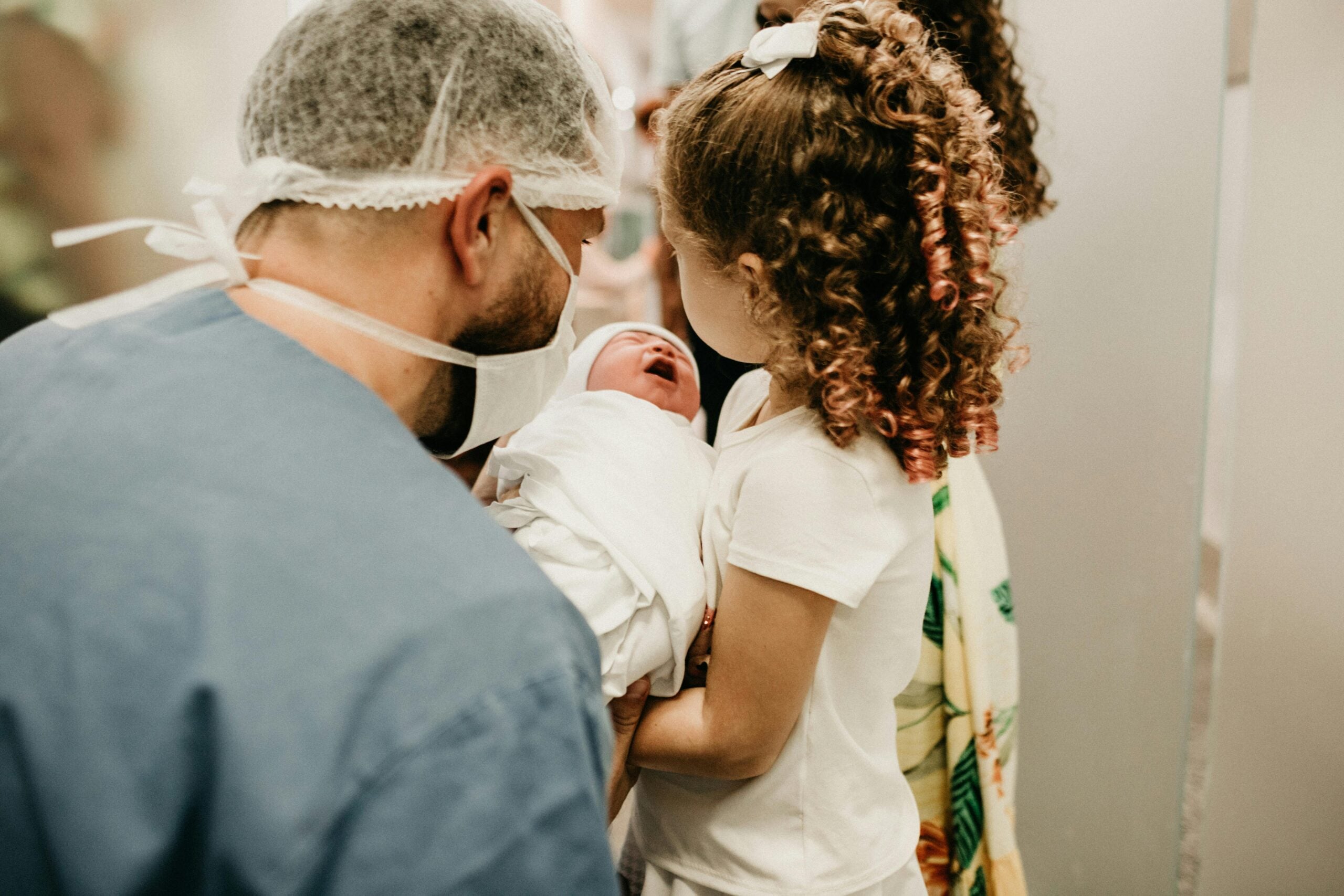 Father and child holding newborn in hospital room, representing neonatal care and injury recovery.

