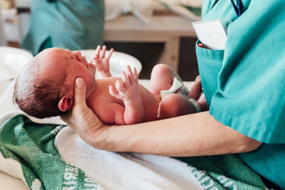 Newborn baby in hospital following oxygen deprivation birth injury, being attended by healthcare staff