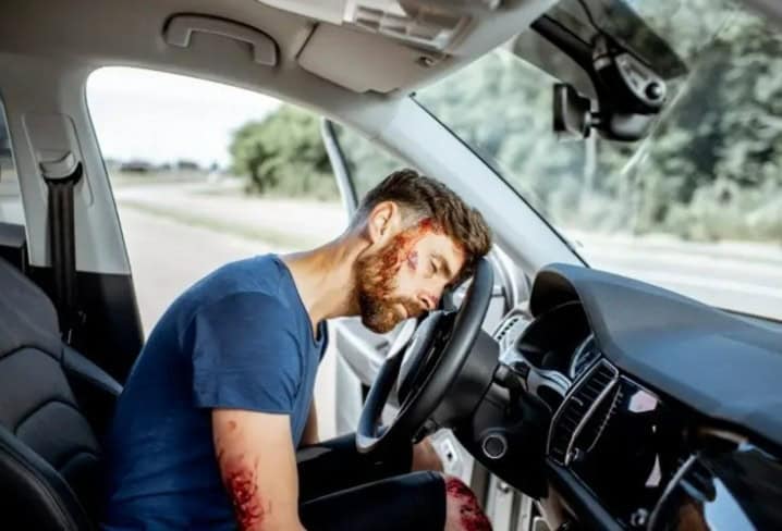 Man injured after truck accident slumped over steering wheel with visible head wounds.