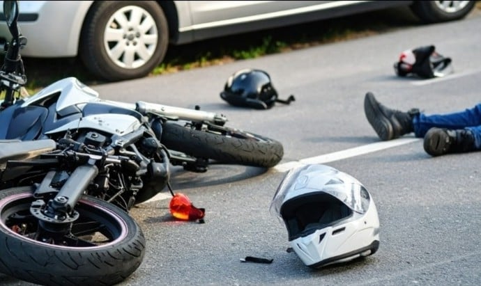 Motorcycle accident scene with fallen bike, helmet on road, and injured rider nearby.