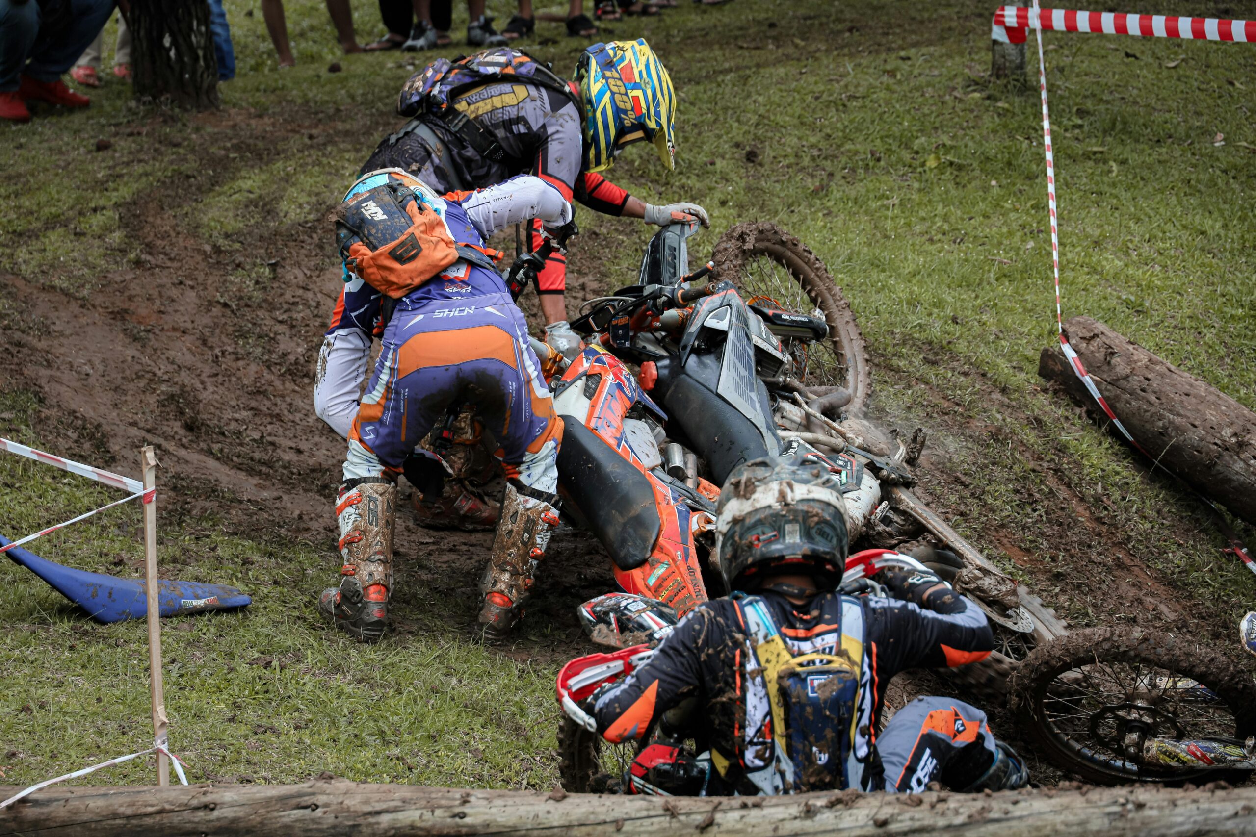 Riders helping recover a crashed dirt bike during a muddy motorcycle race event scene