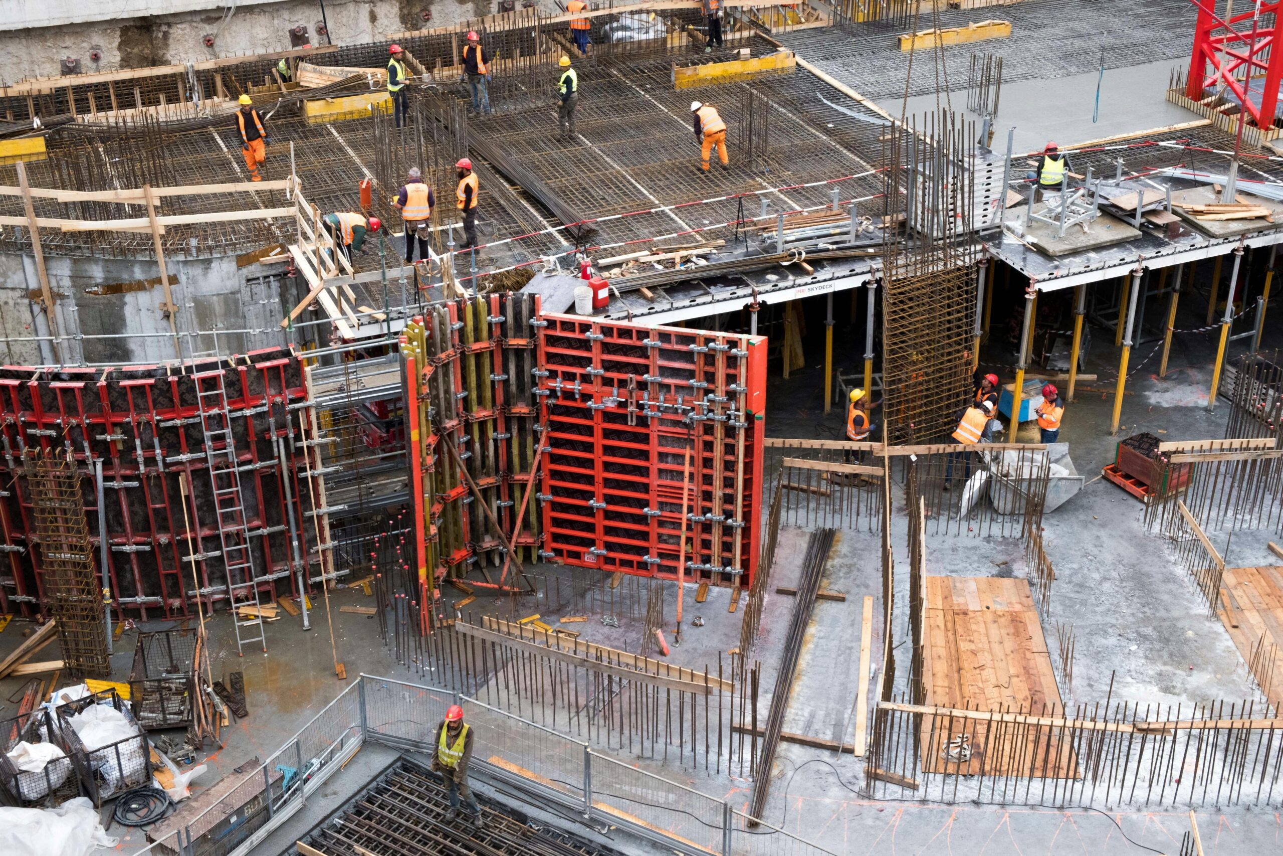 Construction workers pouring concrete and installing steel framework at active urban job site.
