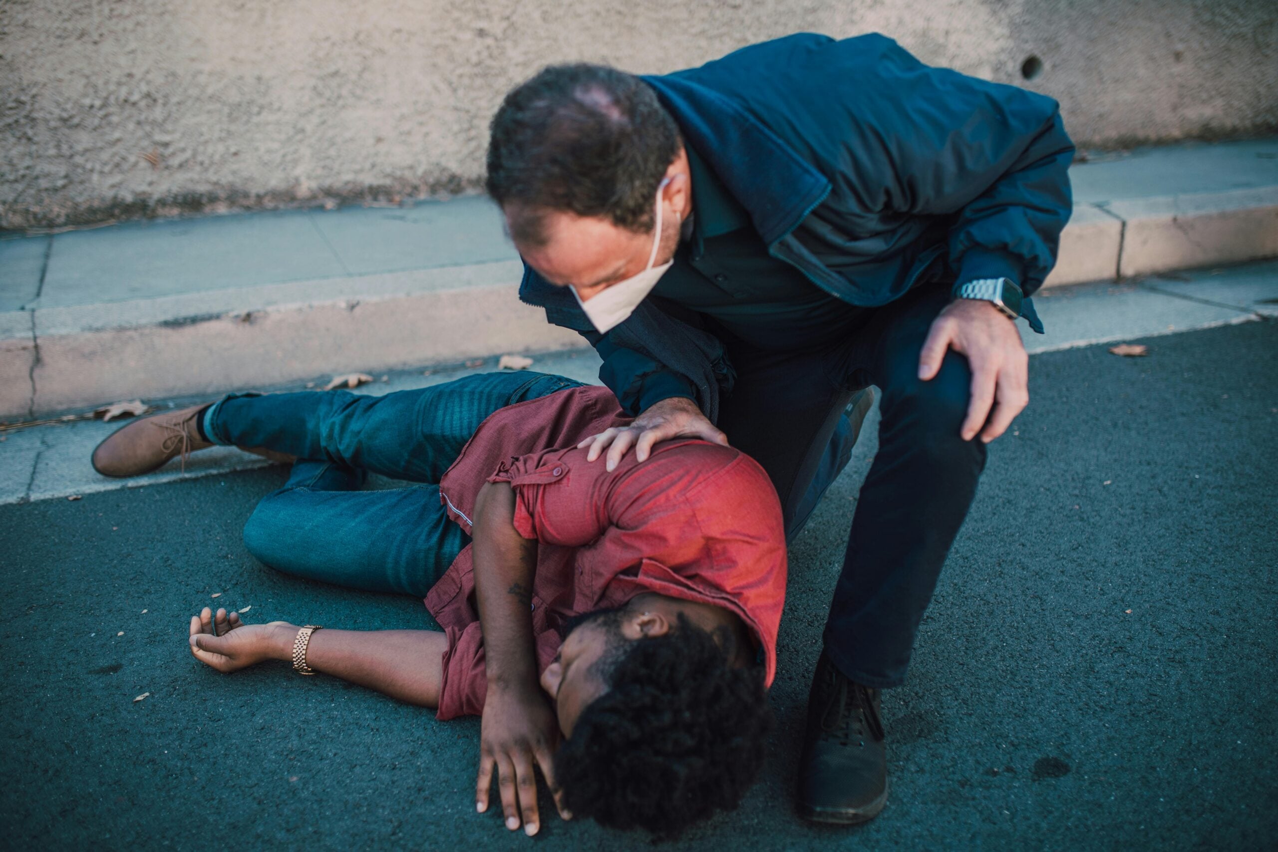 Bystander assisting injured person lying on pavement after possible slip and fall accident.
