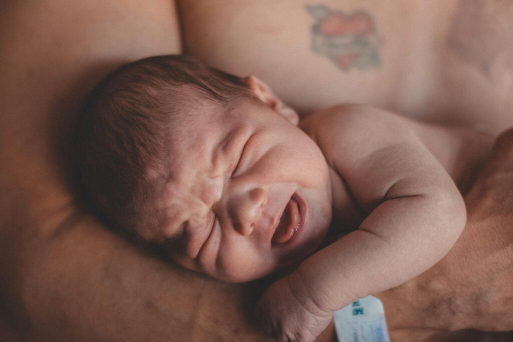Newborn baby in arms, expressing discomfort with a scrunched-up face.