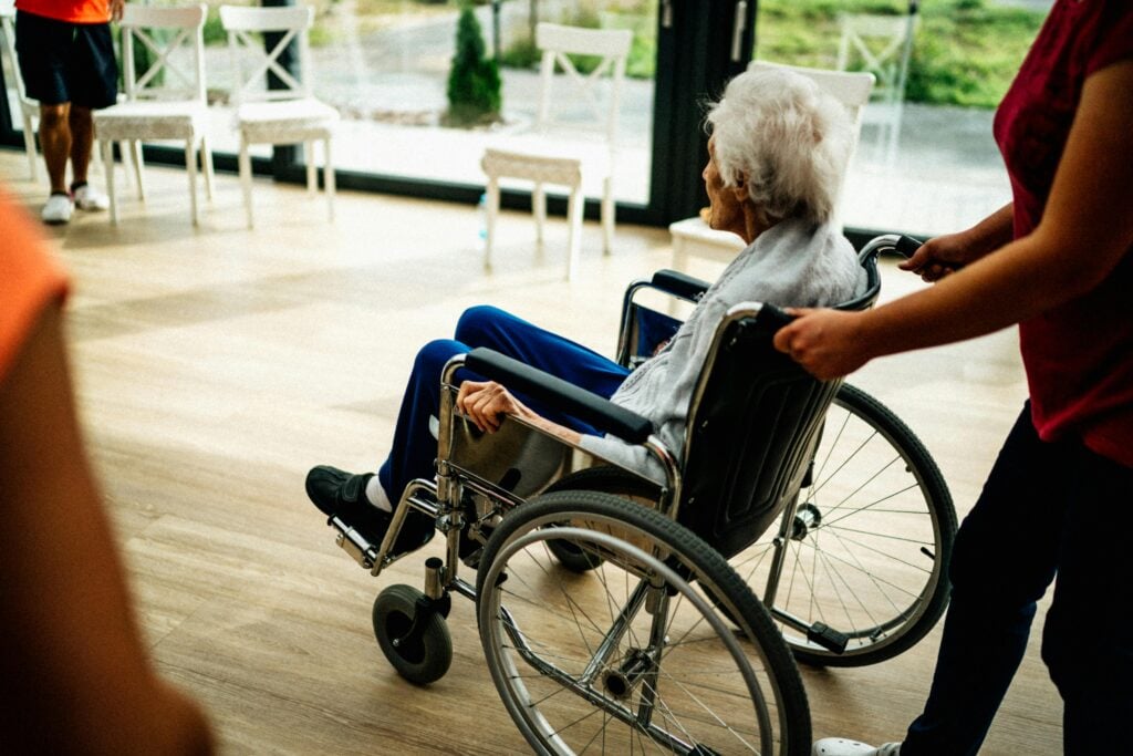 Elderly nursing home abuse victim assisted in wheelchair by caregiver inside Syracuse care facility