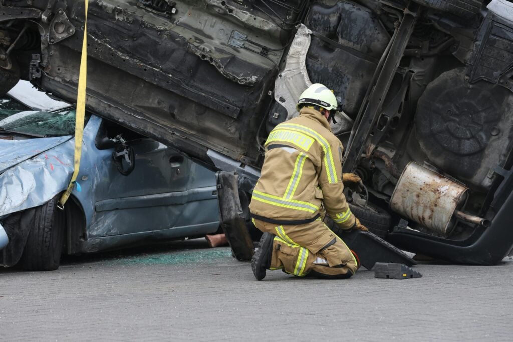 Firefighter responding to severe Syracuse truck accident involving crushed blue sedan on highway crash scene.