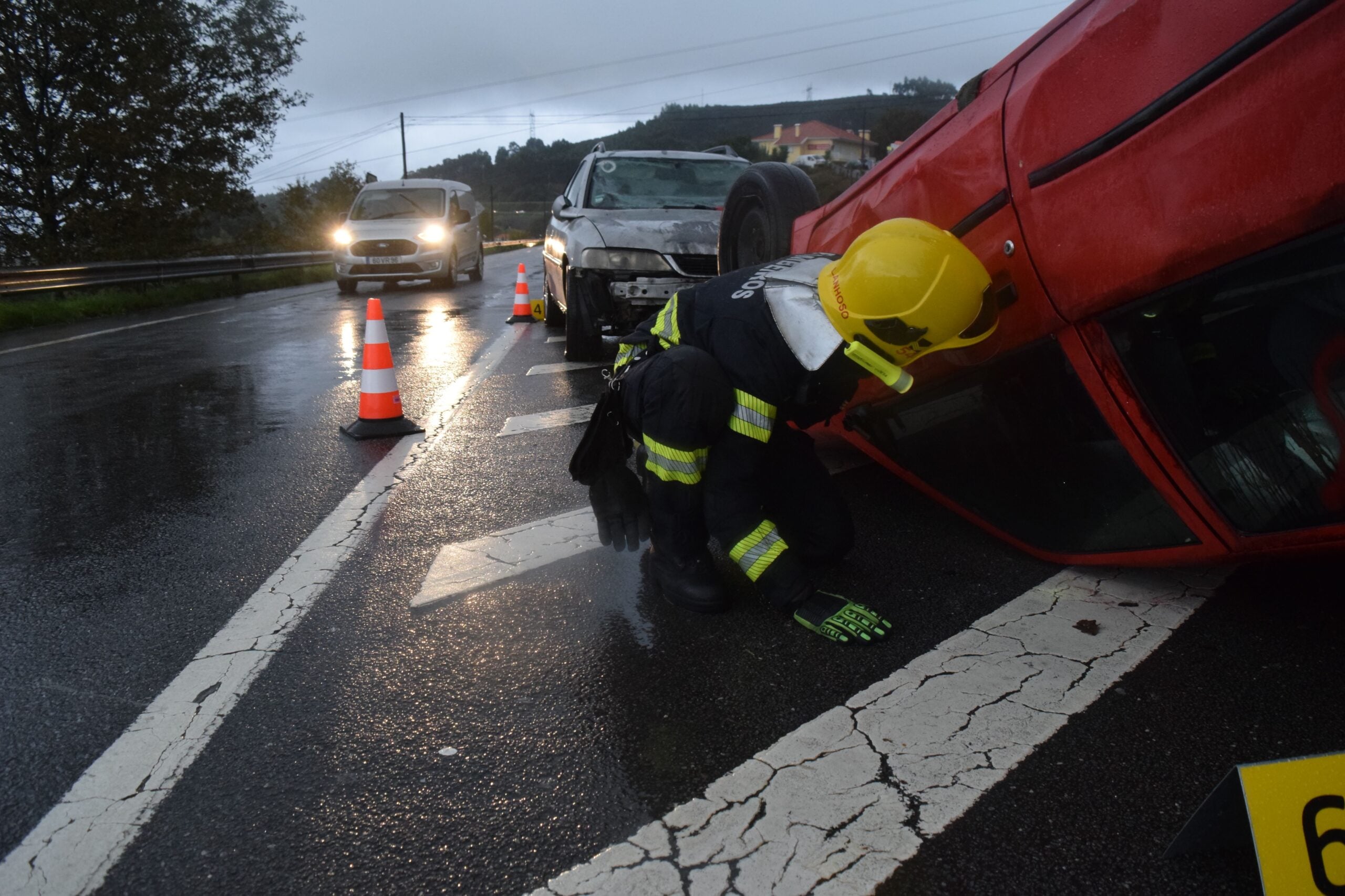 Emergency responder inspects overturned red vehicle at car accident on wet road.