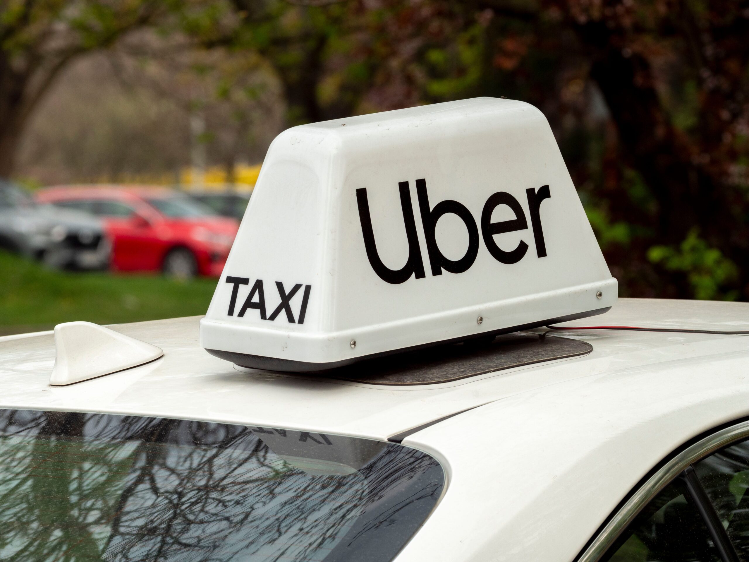 Uber taxi roof sign mounted on a vehicle parked outdoors with blurred cars nearby