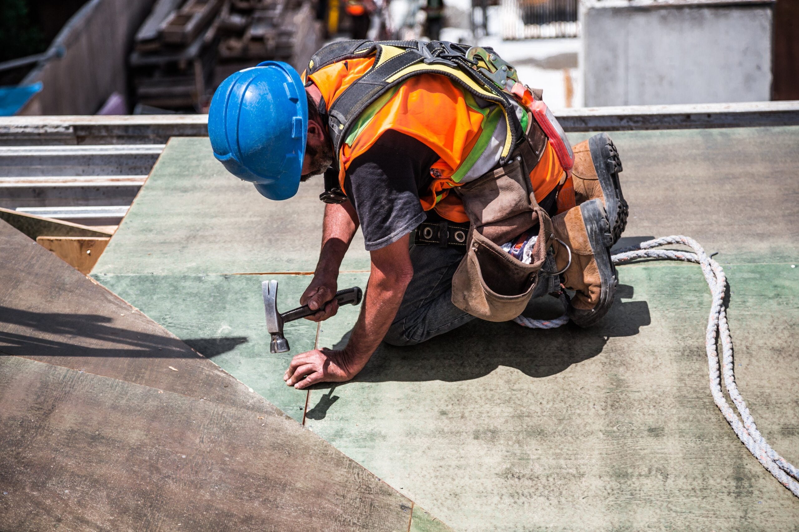 Construction worker kneeling on rooftop surface while securing materials with a hammer